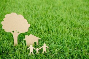 Paper cut of family with house and tree on fresh spring green grass