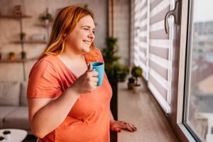 woman-stands-by-window-drinking-coffee